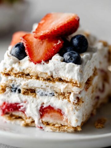 Easy Berry Icebox Cake Recipe 15 Slice of berry icebox cake layered with graham crackers, whipped cream, strawberries, and blueberries on a plate.