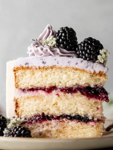 Moist Blackberry Lavender Cake Recipe 14 A slice of Blackberry Lavender Cake layered with blackberry filling and frosted with lavender buttercream, topped with fresh blackberries and decorative flowers.