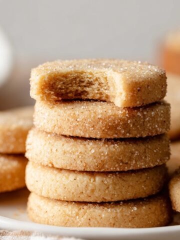 Brown Sugar Shortbread Cookies 13 Brown Sugar Shortbread Cookies with a dusting of sugar on top, showing a bite taken from the top cookie. The warm golden color and smooth texture of the cookies are emphasized.