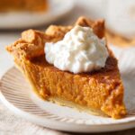 Slice of homemade Brown Sugar Sweet Potato Pie topped with whipped cream on a plate, showing creamy spiced filling and flaky crust.