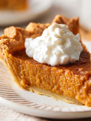 Brown Sugar Sweet Potato Pie 13 Slice of homemade Brown Sugar Sweet Potato Pie topped with whipped cream on a plate, showing creamy spiced filling and flaky crust.