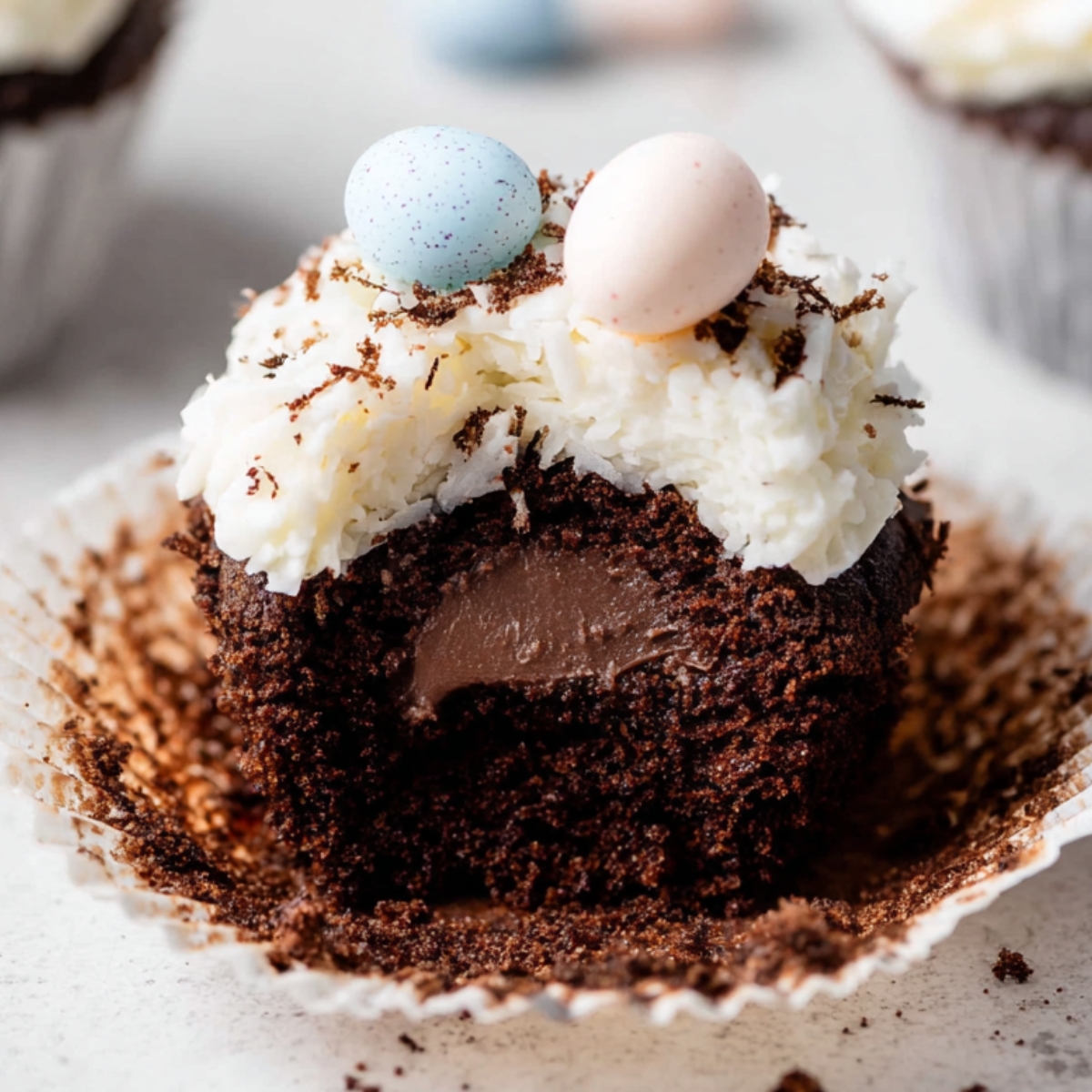 Coconut Chocolate Easter Cupcakes with coconut frosting, pastel candy eggs, and a chocolate ganache filling inside.