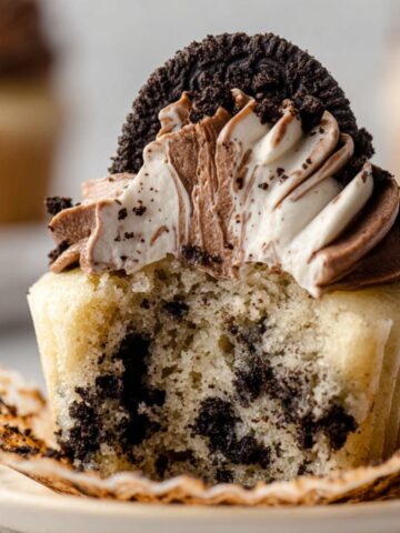 Delicious Cookies and Cream Cupcakes 16 A Cookies and Cream Cupcakes with chocolate and vanilla frosting swirls topped with an Oreo cookie, showing a bite taken out of the cupcake.