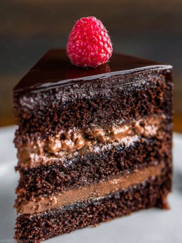 Dark Chocolate Mousse Cake Recipe 16 A close-up shot of a rich, layered Dark Chocolate Mousse Cake with raspberry filling, topped with a fresh raspberry and glossy chocolate glaze.