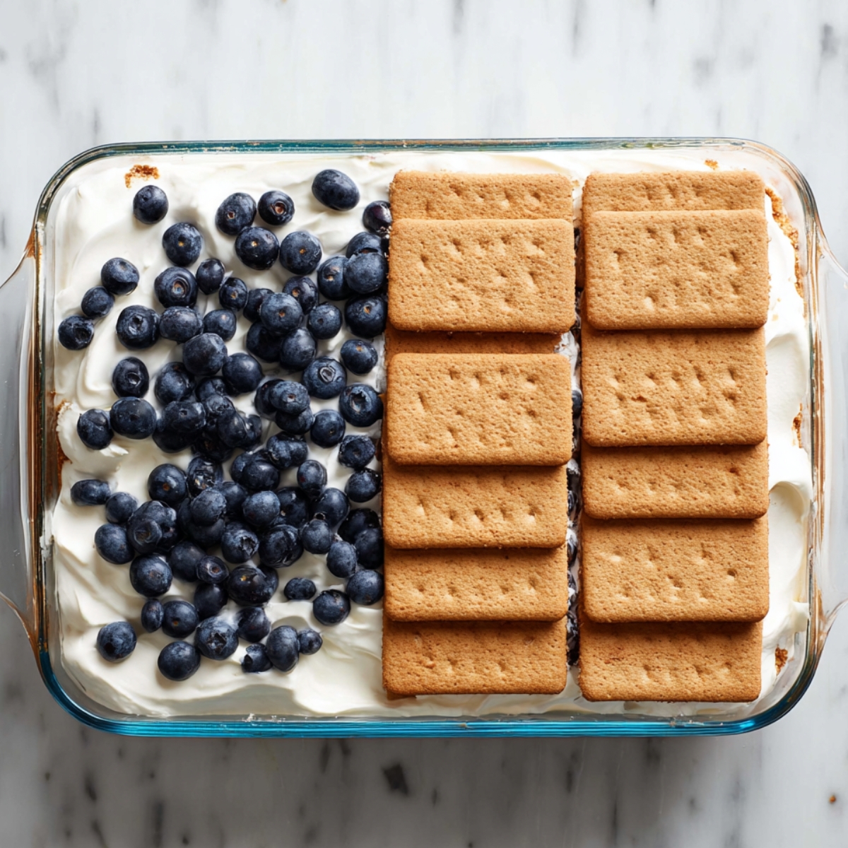 Easy Berry Icebox Cake Recipe 12 Top view of icebox cake in glass dish with a final layer of graham crackers spread over whipped cream.