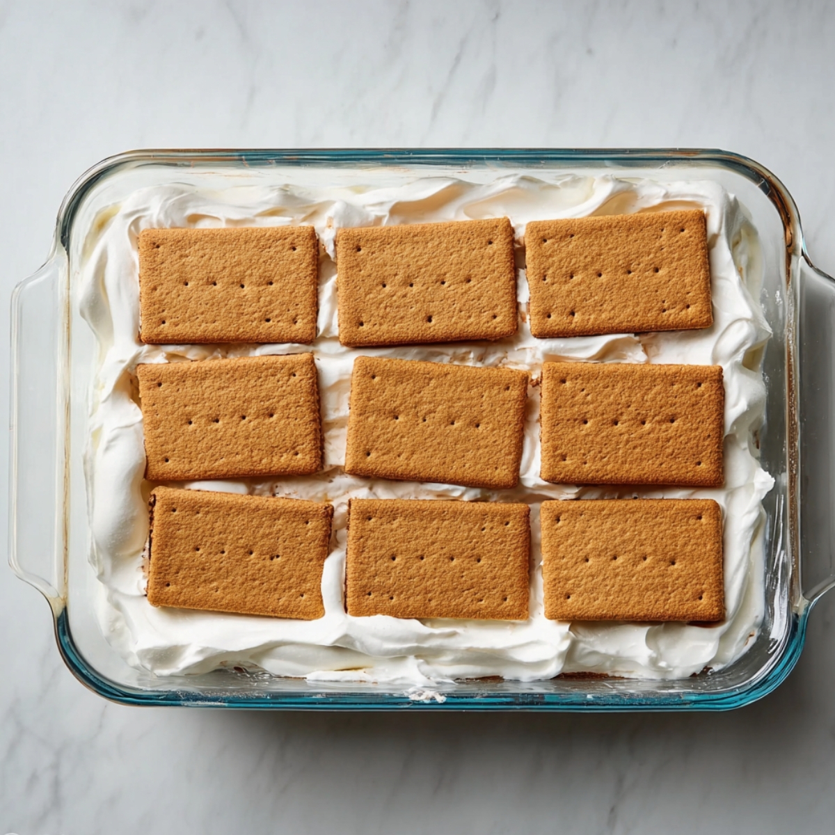 Easy Berry Icebox Cake Recipe 11 First layer of graham crackers arranged over whipped cream in a glass baking dish for icebox cake.