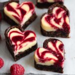 Fudgy Heart Shaped Brownies with a creamy cheesecake topping, swirled with raspberry sauce, creating a beautiful and decadent dessert.