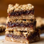 Three homemade oatmeal fig bars stacked neatly. The bars have a golden-brown oat crust with a rich fig filling visible in the middle, showcasing the perfect texture and layers of oats and fig.