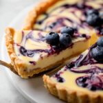 Slice of Lemon Blueberry Tart with swirled blueberry topping and fresh blueberries on a white plate.