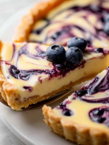 The Best Lemon Blueberry Tart Recipe 4 Slice of Lemon Blueberry Tart with swirled blueberry topping and fresh blueberries on a white plate.