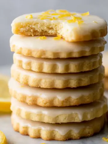 Easy Lemon Shortbread Cookies Recipe 16 A stack of beautifully glazed Lemon Shortbread Cookies, with a bite taken out of the top one, showing the soft, buttery interior.