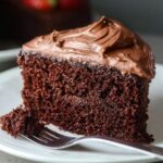 A close-up of a slice of Moist Chocolate Mayonnaise Cake with frosting, sitting on a plate.