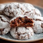 A close-up of freshly baked Nutella Crinkle Cookies with powdery sugar coating, showing a soft and gooey interior with melted Nutella and hazelnuts.