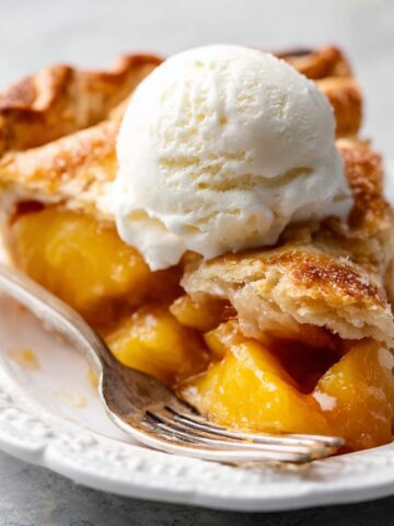 A slice of freshly baked peach pie with a scoop of vanilla ice cream on top.