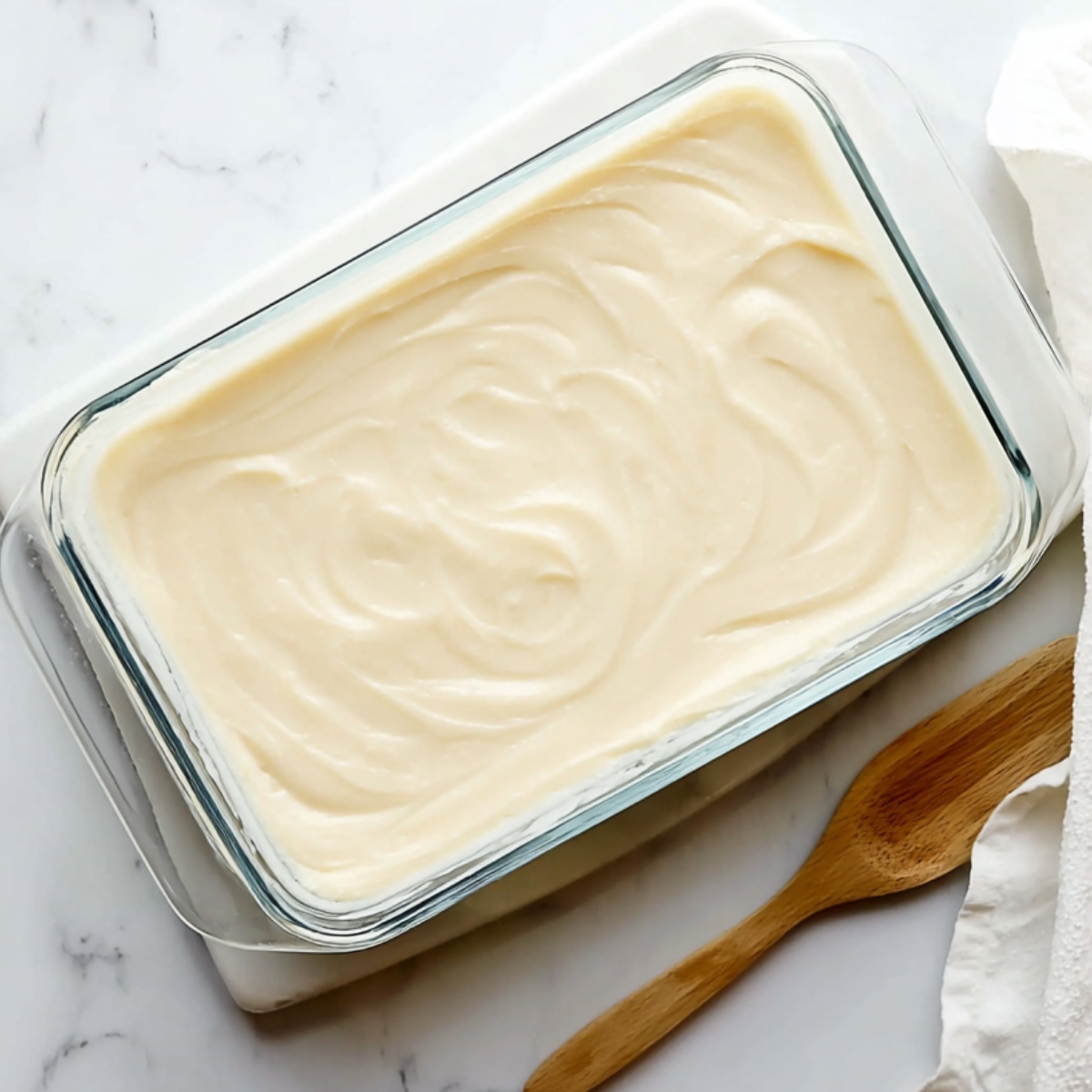 Vanilla Sheet Cake with Whipped Buttercream Frosting 11 Vanilla sheet cake evenly frosted with smooth buttercream in a glass baking dish, spread into decorative swirls before slicing.