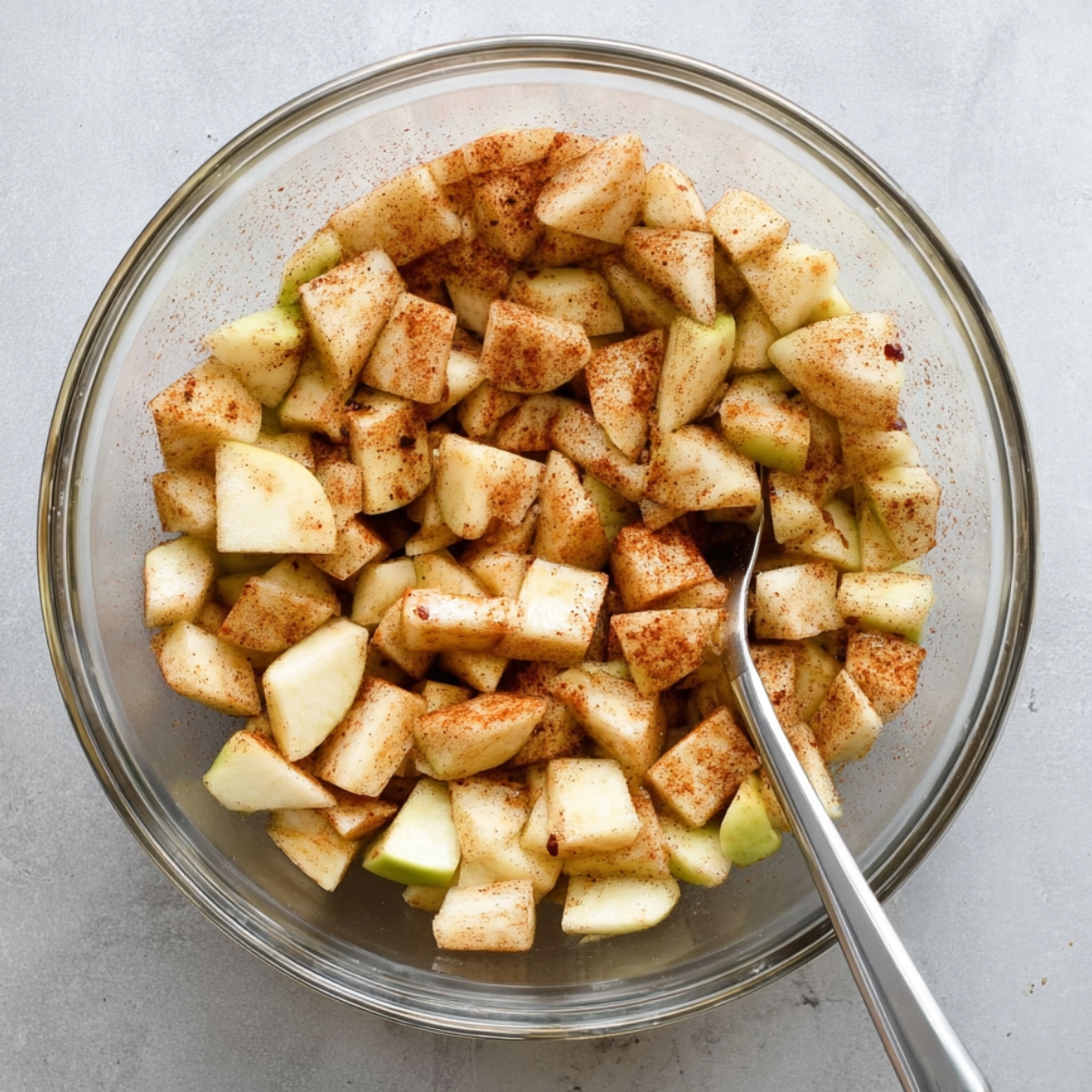 Individual Apple Crumbles Recipe 10 Chopped apples tossed with cinnamon in a glass mixing bowl.