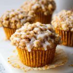 A close-up of a Pumpkin Crumb Cake Muffins Recipe with a crumb topping, sliced in half to reveal the soft and moist interior.