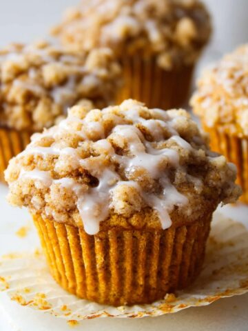 A close-up of a Pumpkin Crumb Cake Muffins Recipe with a crumb topping, sliced in half to reveal the soft and moist interior.