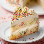 A slice of Sprinkle Cake on a plate with colorful sprinkles on top and visible sprinkles throughout the cake layers.