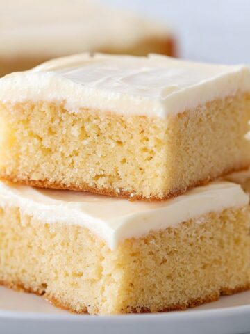 Vanilla Sheet Cake with Whipped Buttercream Frosting 14 Soft vanilla sheet cake squares with smooth buttercream frosting stacked on a plate, showing a moist and fluffy crumb texture.