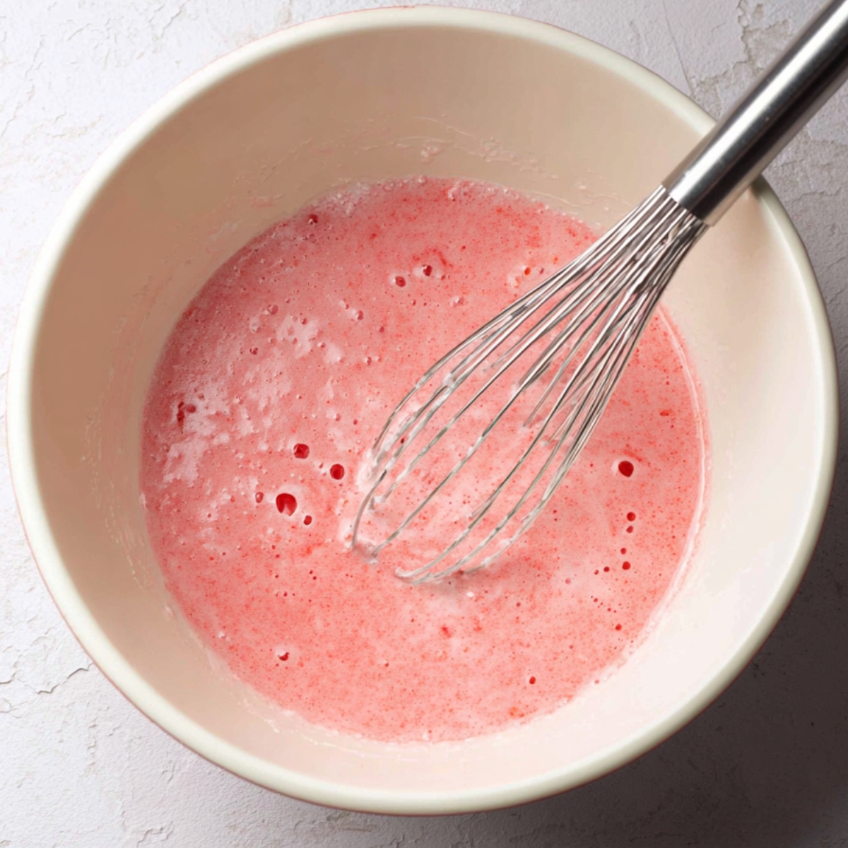 Easy Cherry Chip Cake Recipe 10 A bowl of pink cherry chip cake batter with a whisk inside, showing smooth consistency.