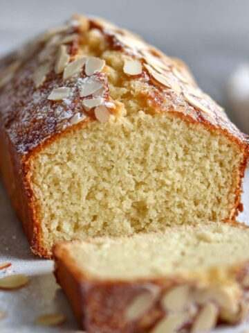 Easy Almond Pound Cake Recipe 2 A freshly baked Almond Pound Cake with a light golden-brown crust, topped with slivered almonds and a dusting of powdered sugar. The cake is sliced to reveal its fluffy, moist texture inside.