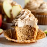 A freshly baked Apple Spice Cupcakes topped with cinnamon-flavored frosting and a slice of fresh apple. The cupcake is cut open to reveal its moist interior.