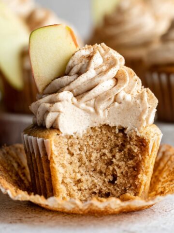 Easy Apple Spice Cupcakes Recipe 1 A freshly baked Apple Spice Cupcakes topped with cinnamon-flavored frosting and a slice of fresh apple. The cupcake is cut open to reveal its moist interior.