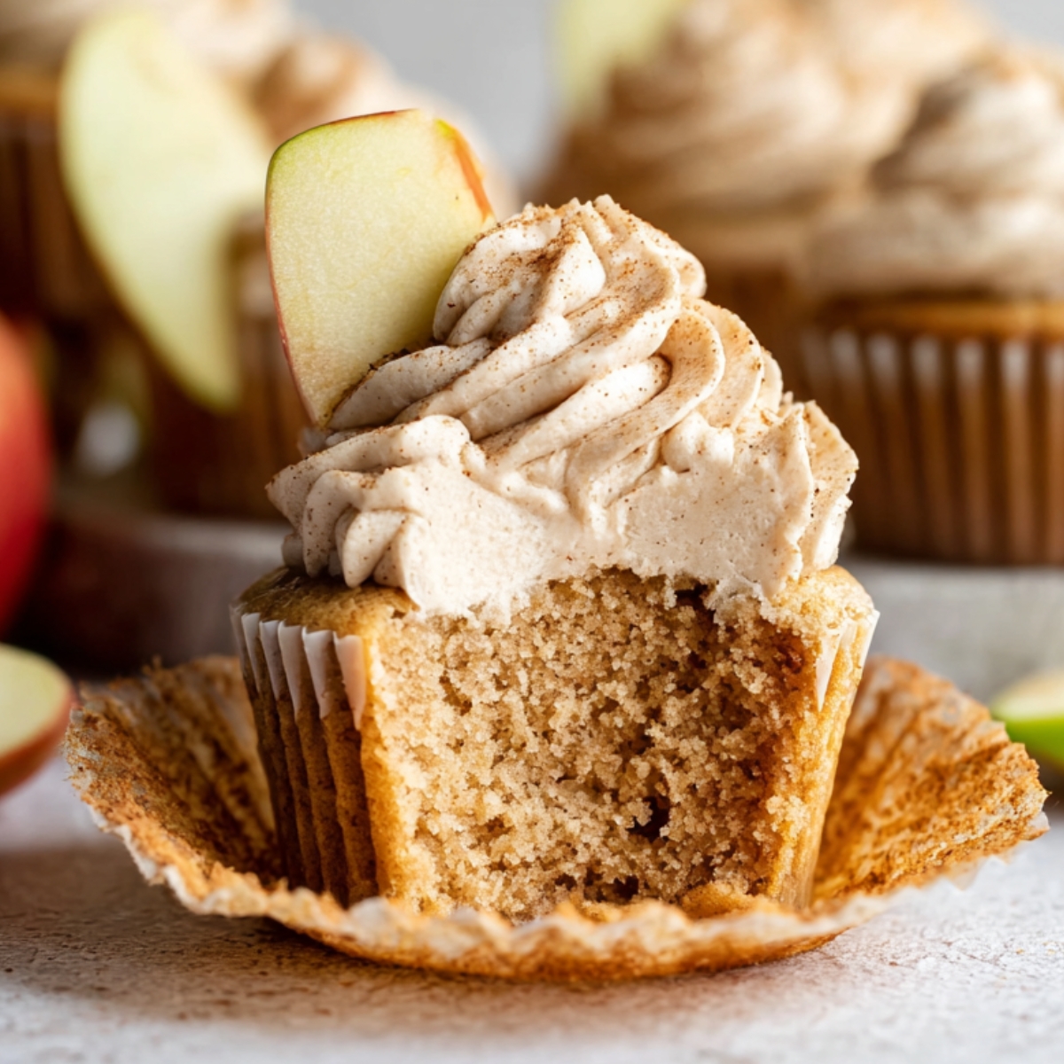 Easy Apple Spice Cupcakes Recipe 9 A freshly baked Apple Spice Cupcakes topped with cinnamon-flavored frosting and a slice of fresh apple. The cupcake is cut open to reveal its moist interior.