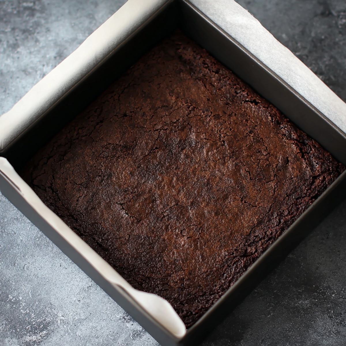 Best Guinness Chocolate Brownies Recipe 12 Freshly baked brownies in a square pan, with a crackled surface and slightly firm edges, cooling down on a marble countertop.