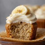 Banana Cupcakes with cream cheese frosting topped with a banana slice and crumbled graham crackers.