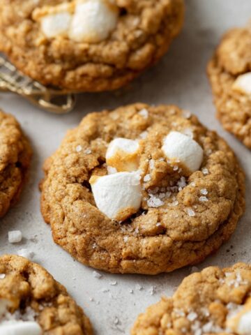 Brown Butter Marshmallow Crispy Cookies 1 Freshly baked Brown Butter Marshmallow Crispy Cookies, golden brown with visible marshmallow chunks, some cookies slightly cracked, sprinkled with a touch of sea salt.