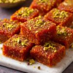 Carrot Burfi pieces garnished with crushed pistachios, served on a white plate.