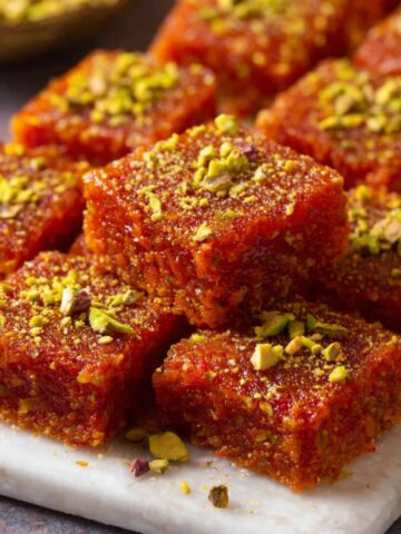 Carrot Burfi (Gajar Pak Recipe) 2 Carrot Burfi pieces garnished with crushed pistachios, served on a white plate.