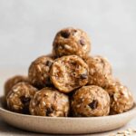 A pile of Chocolate Peanut Butter Protein Balls with one ball cut open, showing the texture of oats and chocolate chips.