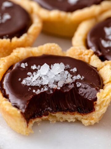 The Best Chocolate Tartlets Recipe 1 A close-up of a Chocolate Tartlets filled with smooth ganache, topped with a sprinkle of sea salt, with a bite taken out showing the creamy interior.