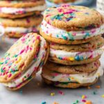 Funfetti Cookie Sandwiches filled with creamy frosting, the cookies are rolled in rainbow sprinkles, giving them a playful and colorful appearance.