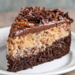 A slice of German chocolate cheesecake topped with pecans, coconut, and chocolate frosting.