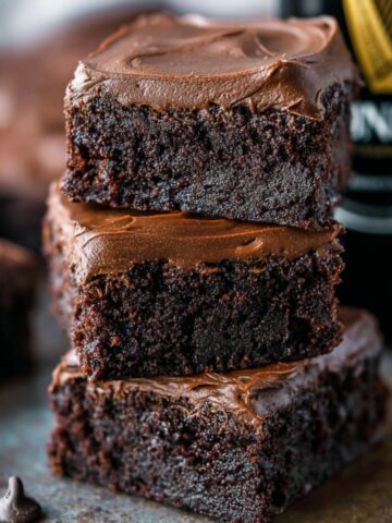 Best Guinness Chocolate Brownies Recipe 3 A stack of decadent Guinness Chocolate Brownies, topped with a smooth layer of chocolate ganache. The brownies have a moist, fudgy texture and are decorated with chocolate chips.