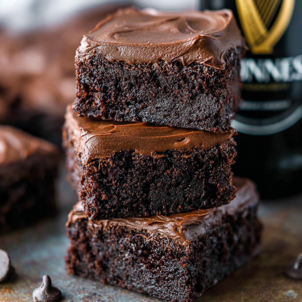 Best Guinness Chocolate Brownies Recipe 9 A stack of decadent Guinness Chocolate Brownies, topped with a smooth layer of chocolate ganache. The brownies have a moist, fudgy texture and are decorated with chocolate chips.