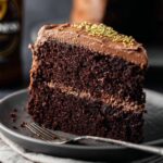 A slice of Guinness Chocolate Cake with smooth chocolate frosting and golden sprinkles on top. The rich, dark cake layers are moist, and the frosting is beautifully spread between the layers.