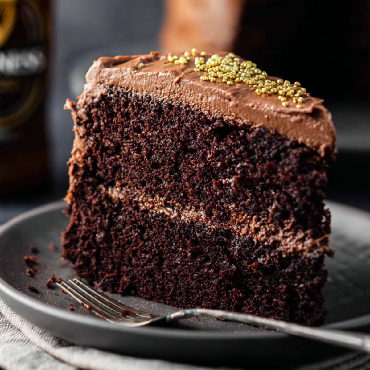 A slice of decadent Guinness chocolate cake with smooth chocolate frosting and golden sprinkles on top. The rich, dark cake layers are moist, and the frosting is beautifully spread between the layers.