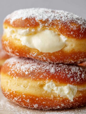 Homemade Bavarian Cream Donuts 2 A stack of sugar-coated Homemade Bavarian Cream Donuts, with a generous filling of cream peeking through the center.
