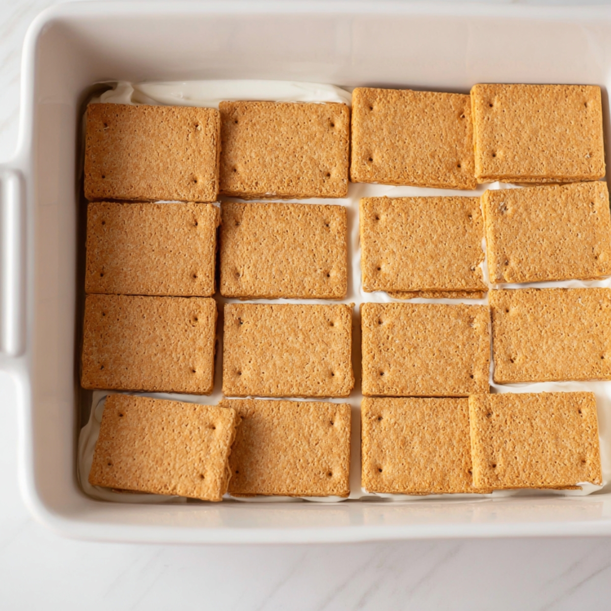 Easy Strawberry Icebox Cake Recipe 10 A dish of graham crackers arranged in a pan, ready for the first layer of a strawberry icebox cake.