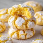 Stacked Lemon Crinkle Cookies with a bite taken out of the top one, showcasing their cracked and sugar-coated exterior with a soft, fluffy interior.