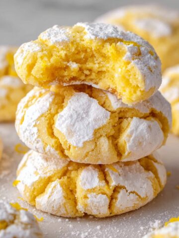Easy Lemon Crinkle Cookies Recipe 2 Stacked Lemon Crinkle Cookies with a bite taken out of the top one, showcasing their cracked and sugar-coated exterior with a soft, fluffy interior.