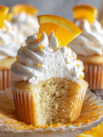 The Best Mimosa Cupcakes Recipe 1 A cut Mimosa Cupcakes showing a soft and fluffy inside, topped with whipped cream, orange zest, and an orange slice.