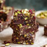 A close-up of stacked No Bake Superfood Brownies, studded with pistachios and dried cranberries, offering a rich, nutrient-packed treat.