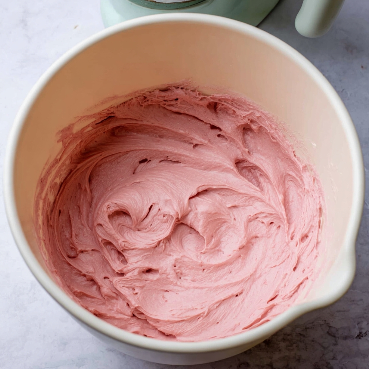 Delicious Strawberry Bundt Cake Recipe 11 Smooth, creamy pink strawberry frosting in a mixing bowl, ready to be used for glazing or frosting cakes and cupcakes.