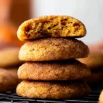 Soft and chewy Pumpkin Snickerdoodles cookies, coated in cinnamon-sugar, with a bite taken out to reveal their fluffy, spiced interior.